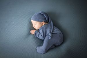 Small baby in blue sleeper naps on dark background.