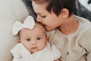 A tender moment between siblings as a baby rests on a white couch.