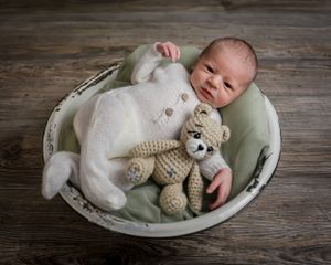 Sleeping newborn baby in white outfit with knit teddy bear in vintage basin.