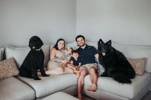 Family relaxing on grey sectional sofa with two black pets.