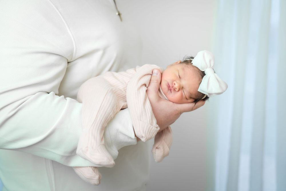 Newborn baby wearing white clothing lies sleeping on white bedding in a series of peaceful poses.