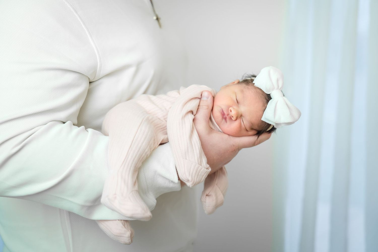 Newborn baby wearing white clothing lies sleeping on white bedding in a series of peaceful poses.