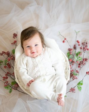 Baby in white sweater laying on tulle fabric with pink cherry blossom branches.