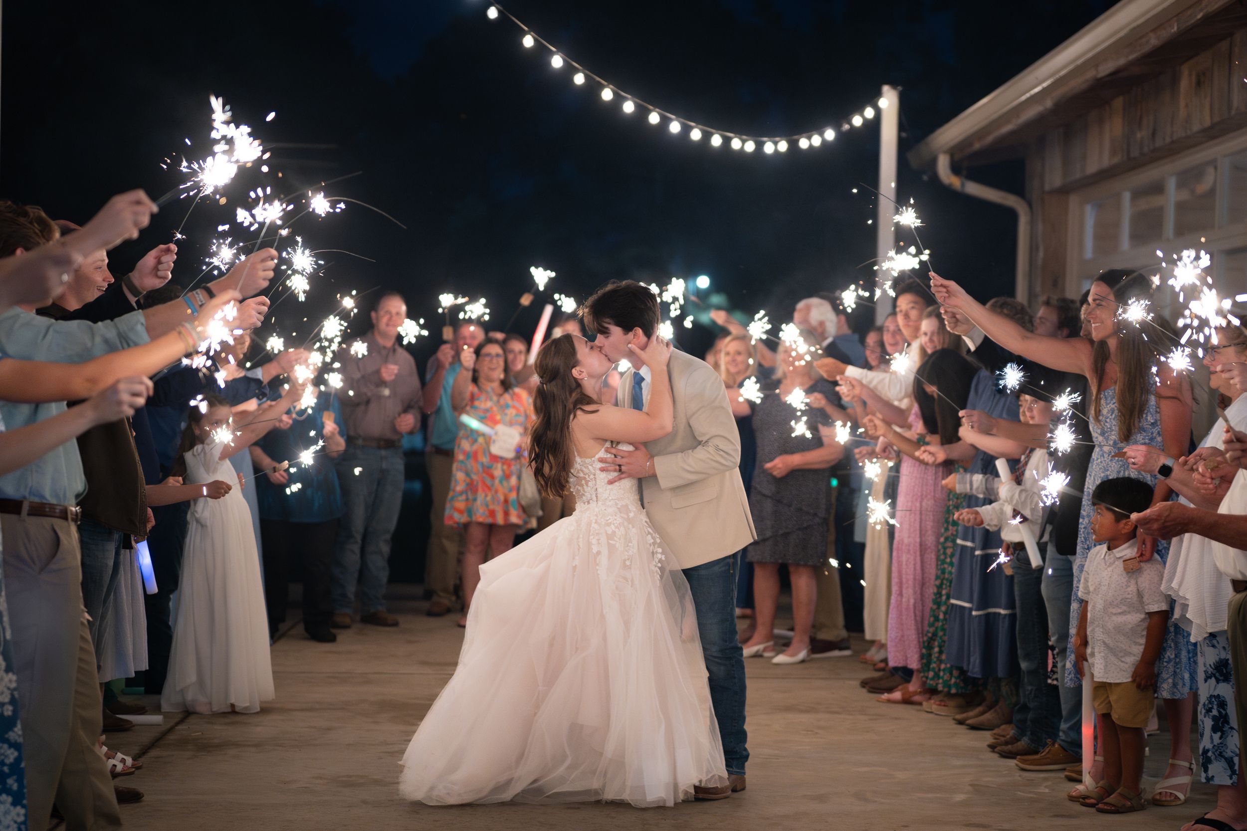 Guests hold sparklers creating a magical tunnel of light as newlyweds walk through during an evening wedding exit.
