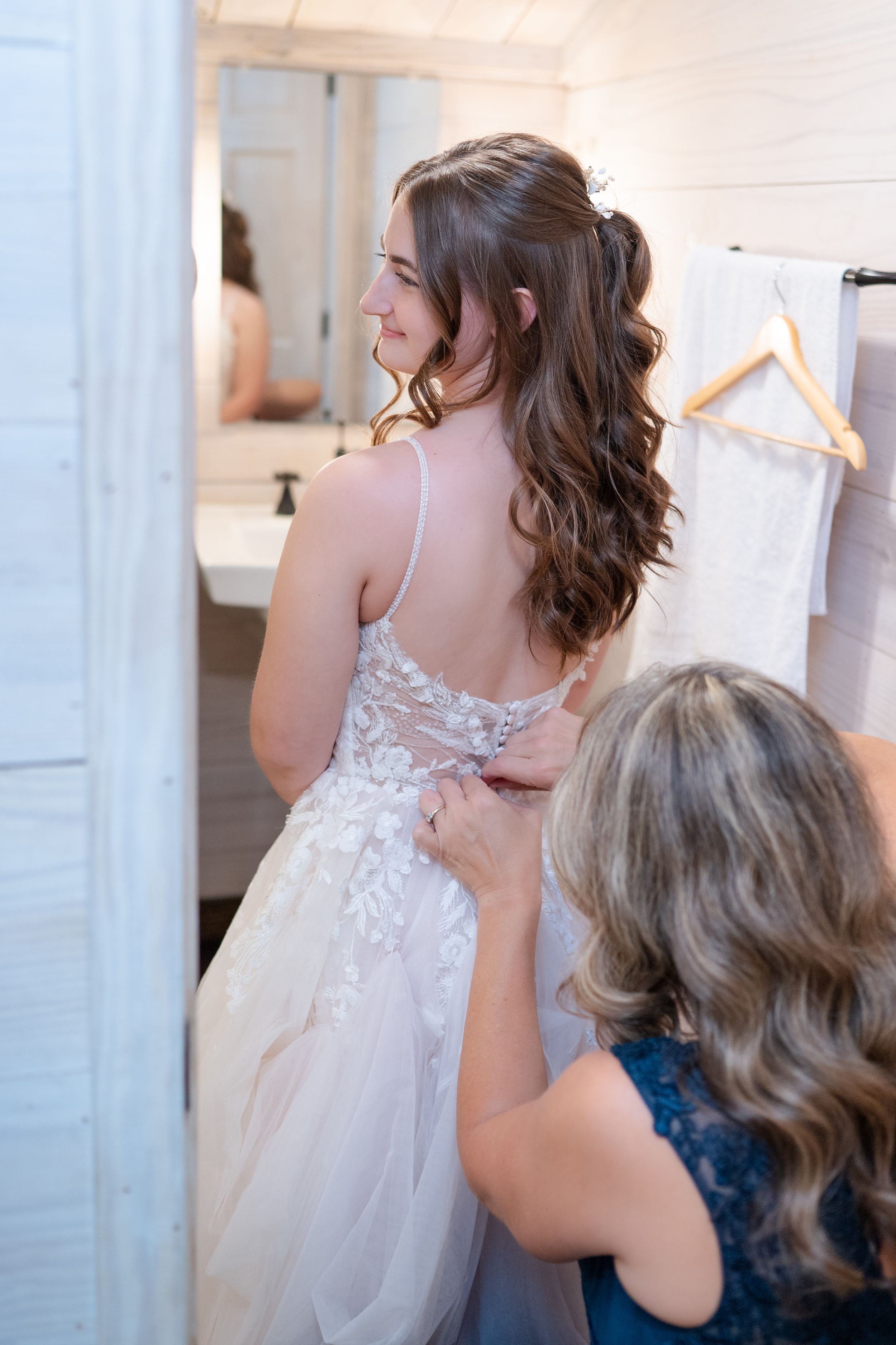 Beautiful lace wedding dress being adjusted in a dressing room with mirror and hanger visible.