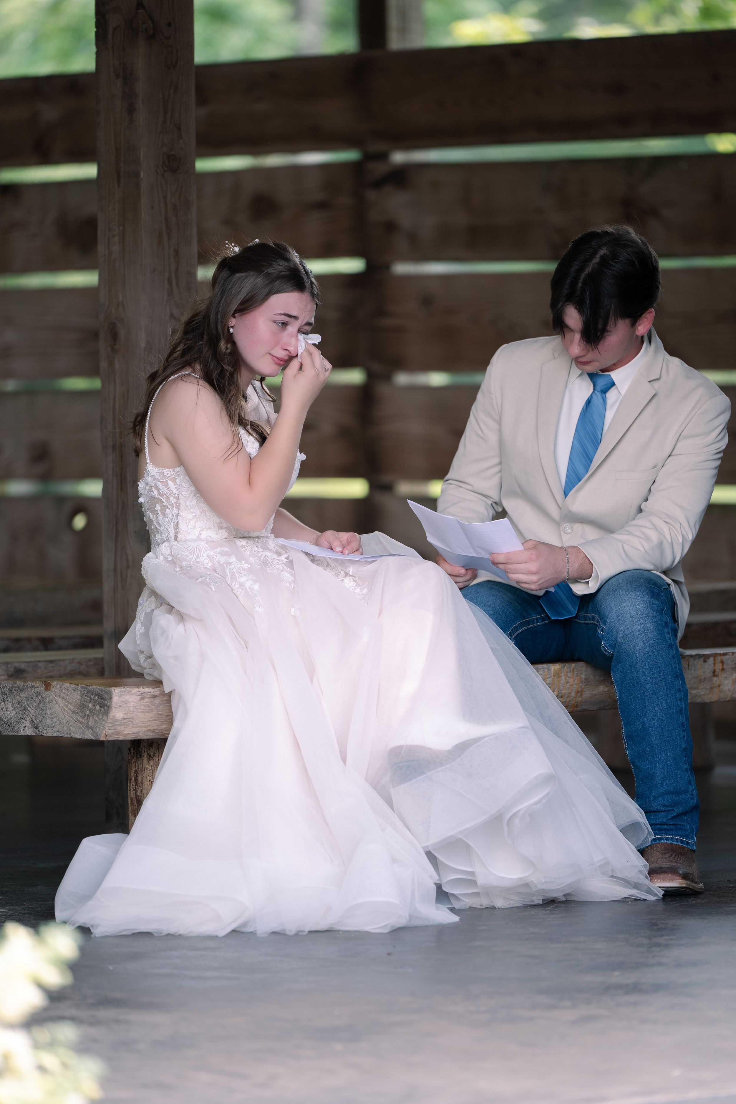 Couple sharing an emotional moment while reading vows together in a rustic wooden structure.