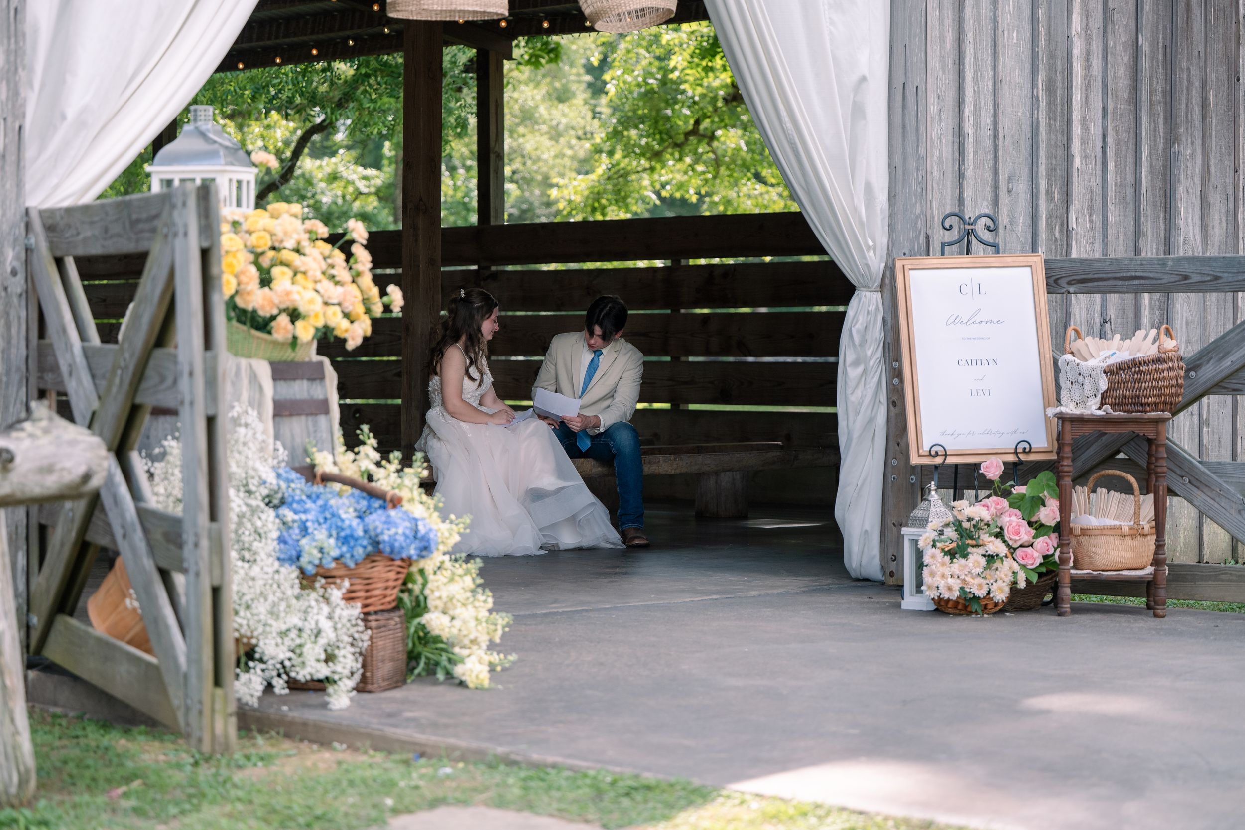 A rustic barn venue decorated with white curtains, floral arrangements and vintage furniture creates a romantic wedding setting.
