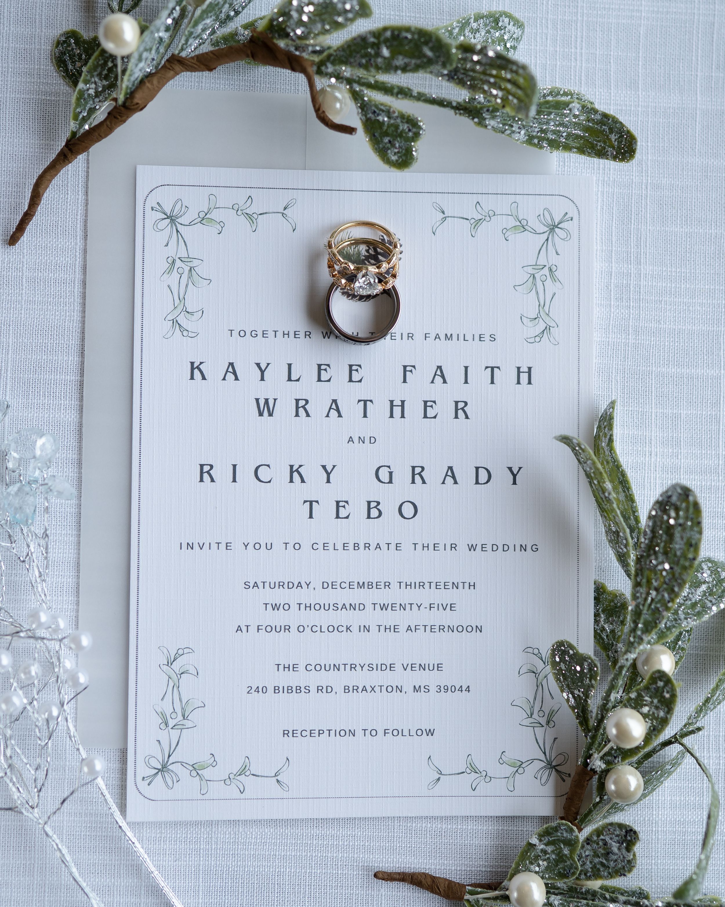 Elegant wedding invitation with floral greenery and white berries on a light gray background.
