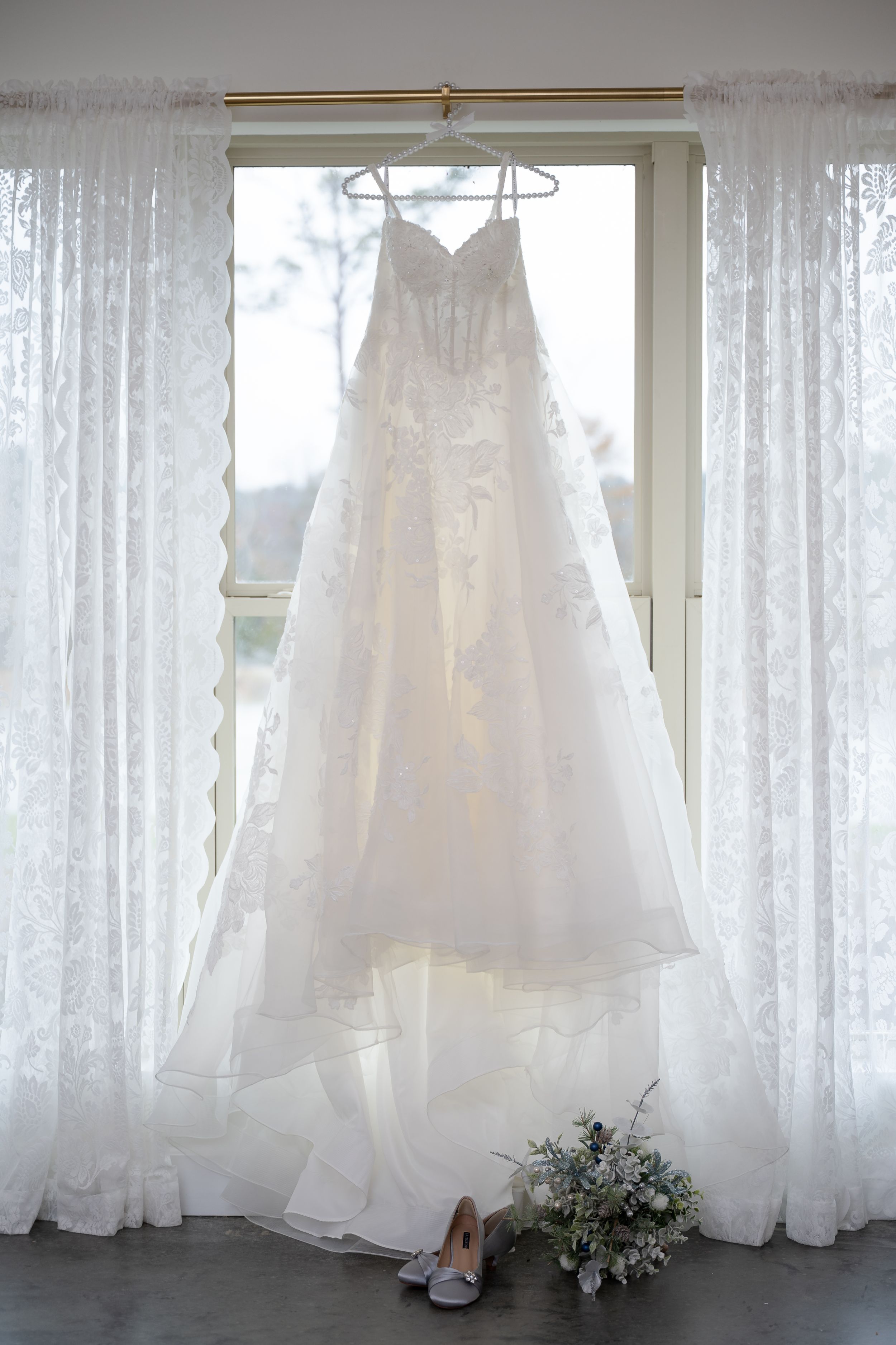 Multiple white wedding dresses hanging on display against sheer curtains in a bridal boutique.