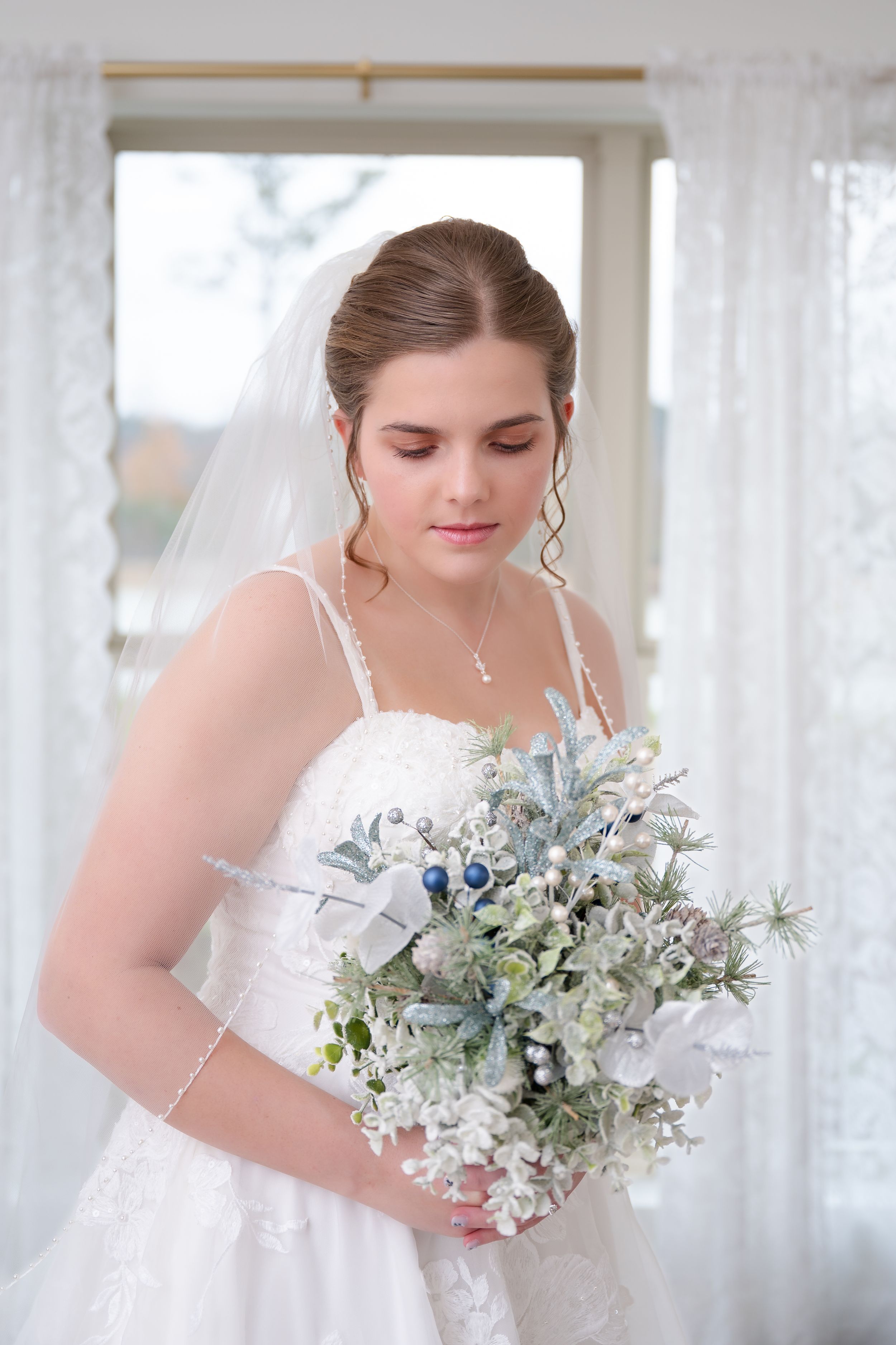 Elegant bride in white lace gown holding a soft blue and white bouquet with eucalyptus accents.