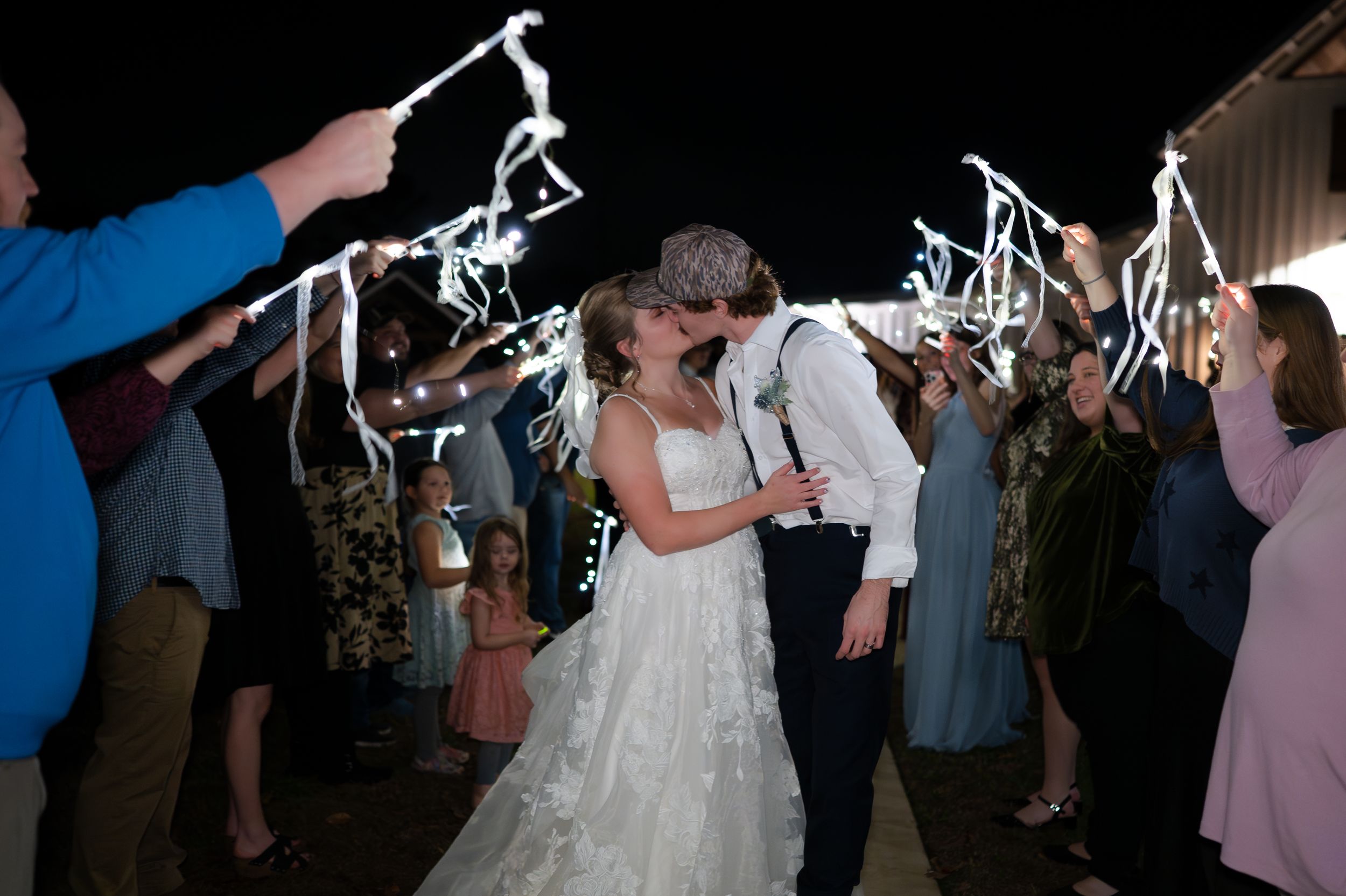 Wedding couple shares romantic moment under sparklers held by guests during evening reception celebration.