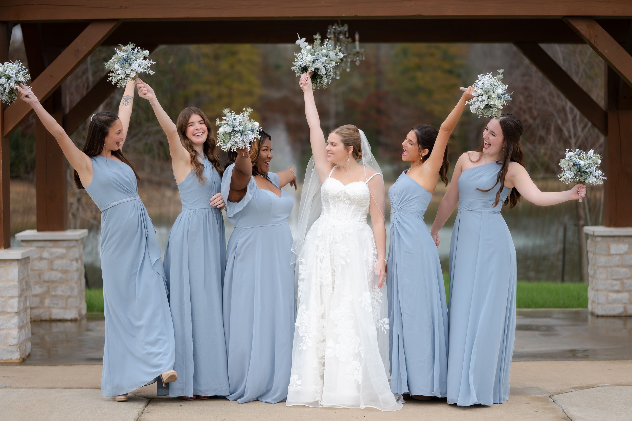 Wedding party in light blue bridesmaid dresses and white bridal gown pose together in outdoor celebration photos.