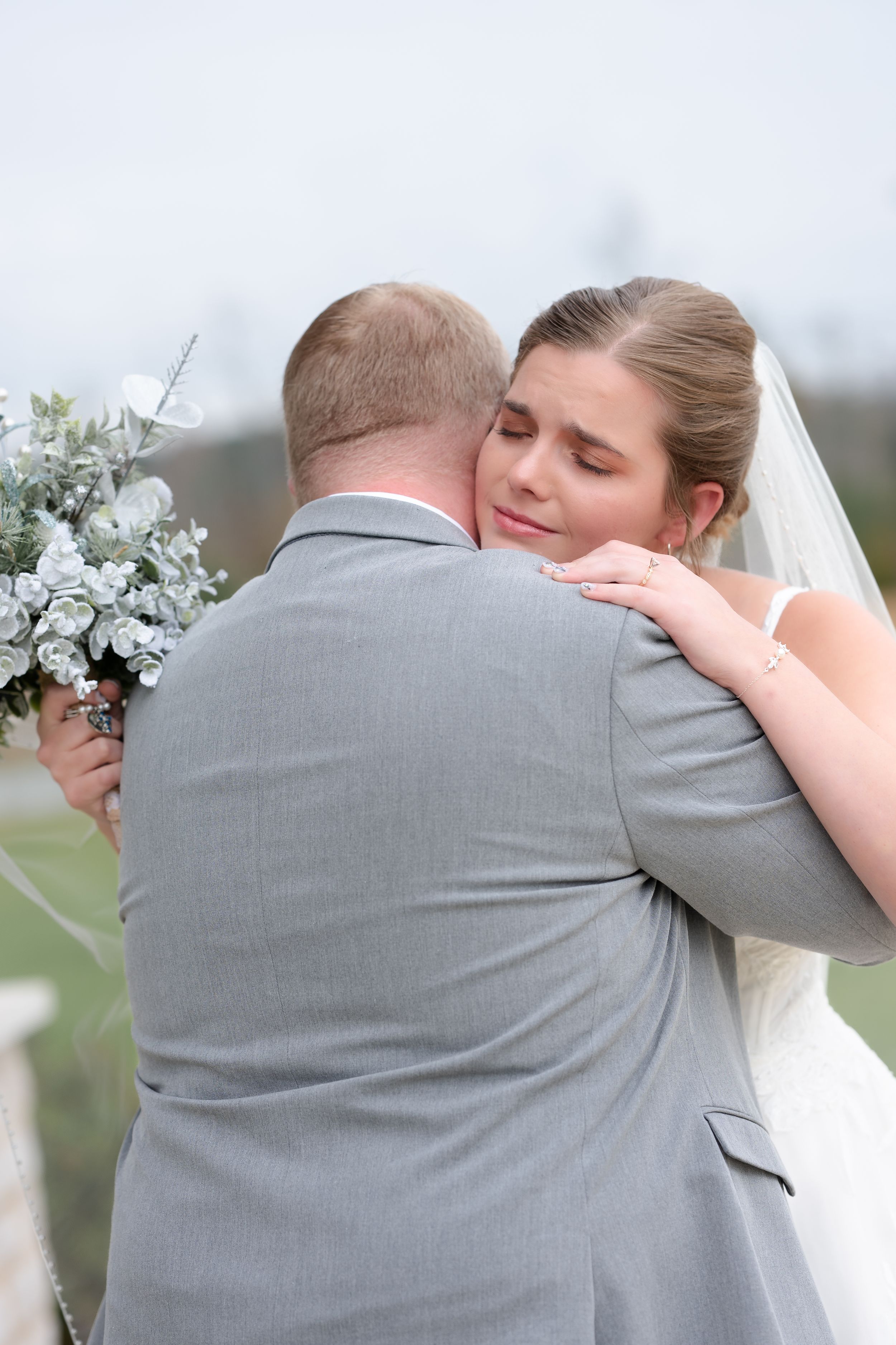 A tender embrace between newlyweds at an outdoor wedding ceremony with white floral bouquet details.