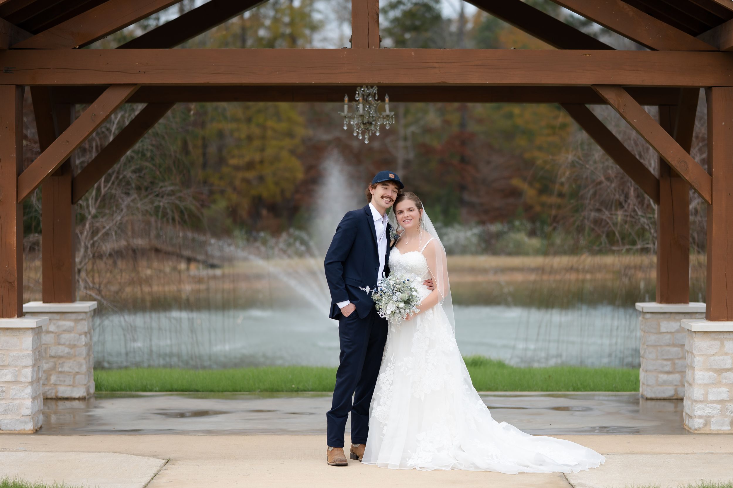Couple shares a romantic moment under a rustic wooden pavilion during an outdoor wedding ceremony.