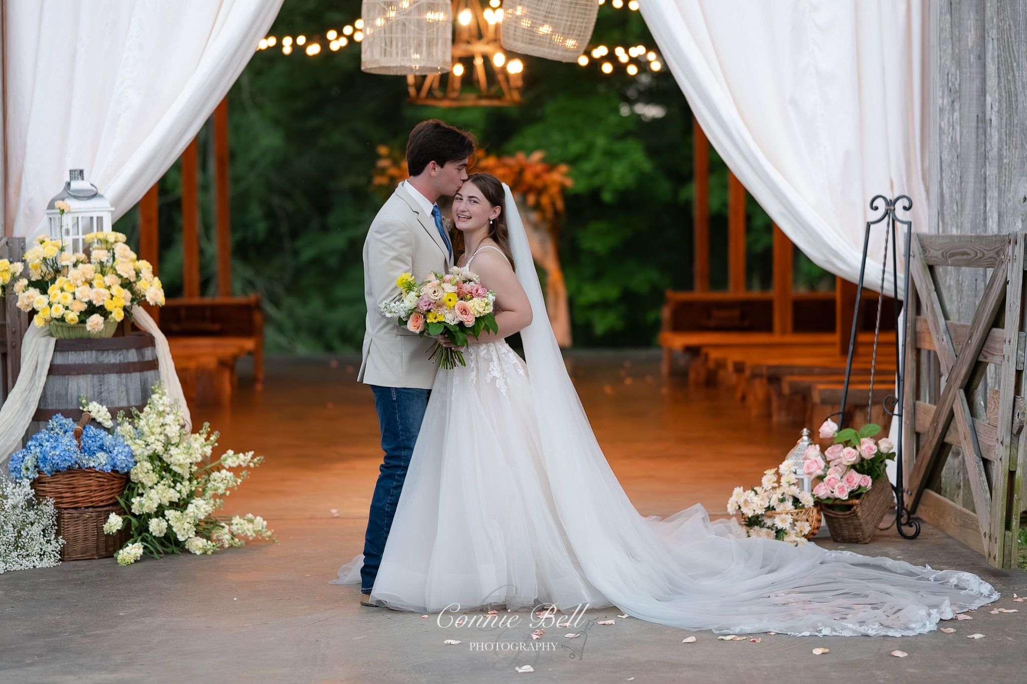 An intimate wedding ceremony in a rustic barn venue decorated with white drapes, florals and twinkling lights.