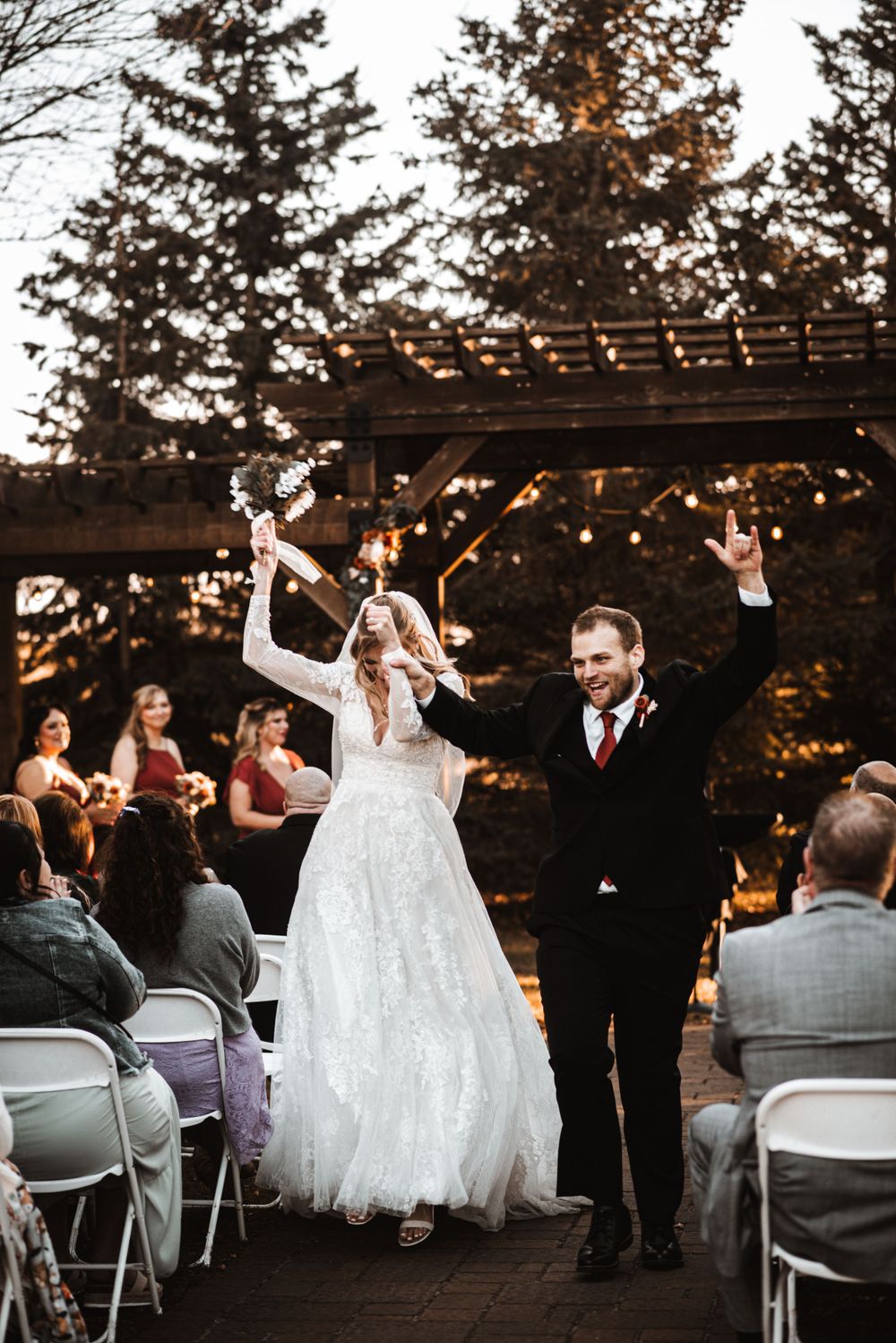 Newlyweds celebrate with raised arms during their outdoor ceremony recessional.