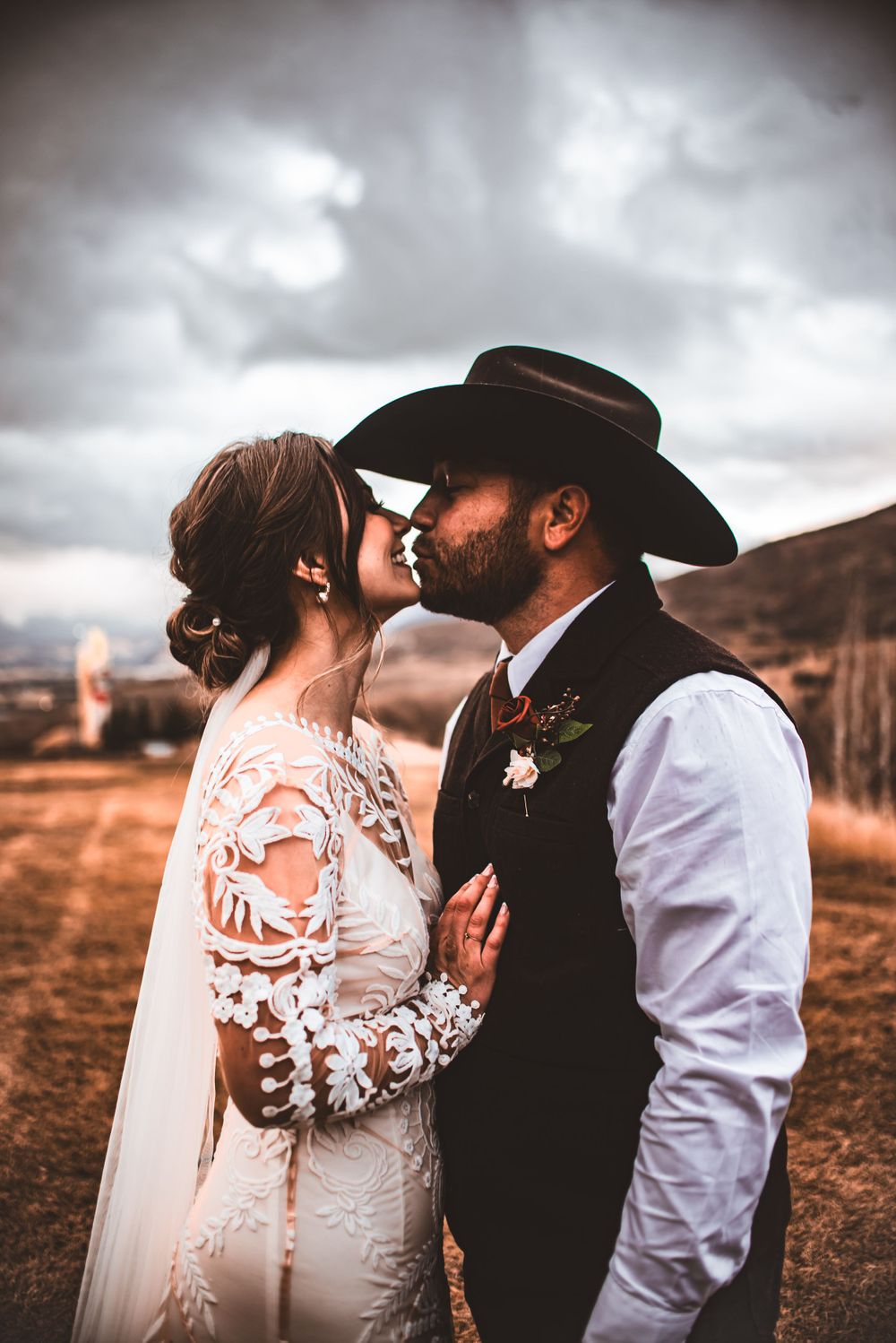 A romantic western wedding kiss set against dramatic cloudy skies and desert landscape.