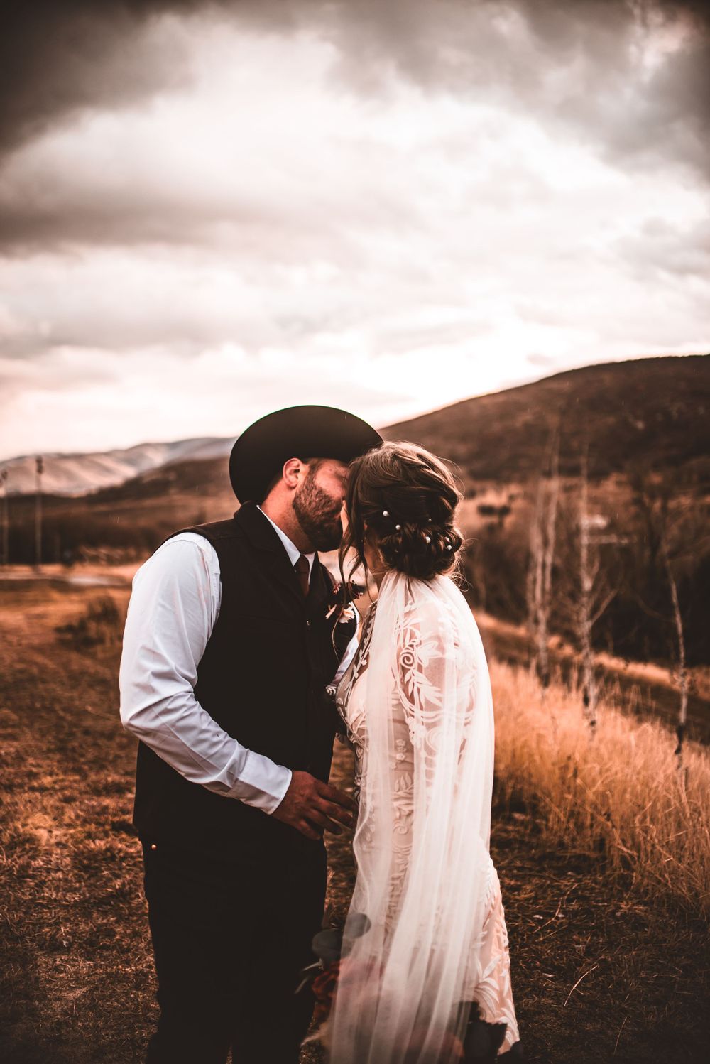 Western-themed wedding couple embraces in front of rustic mountain scenery.