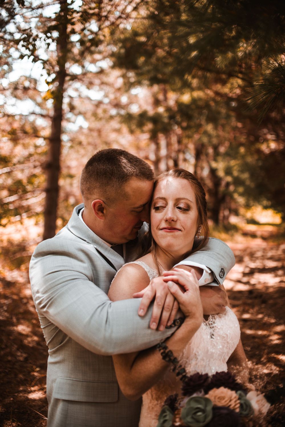 An intimate embrace between newlyweds in a sunlit forest setting with warm autumn colors.
