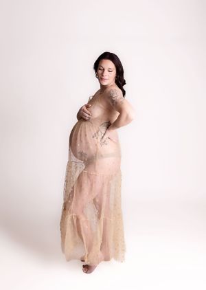 Artistic maternity portrait featuring flowing sheer beige lace gown against neutral studio backdrop.