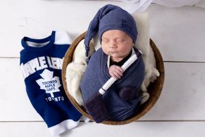 A newborn baby wearing a navy blue outfit lies peacefully in a wooden bowl during a photography session.
