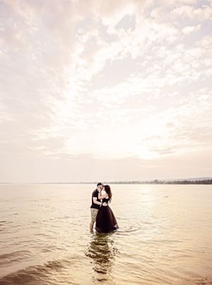 A couple standing together in shallow ocean water during sunset with a dreamy, romantic atmosphere.