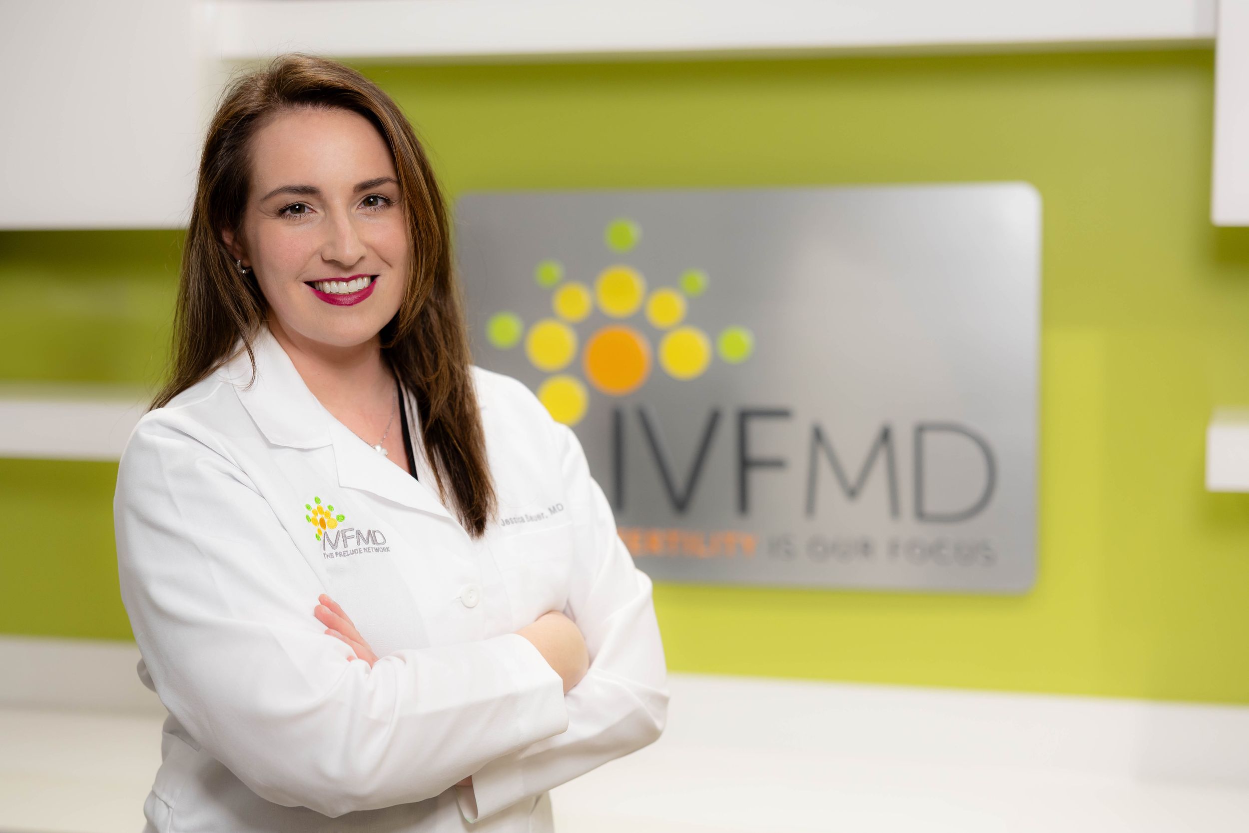 Medical professional in white lab coat smiling against lime green wall with office branding.