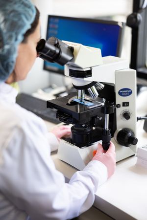 Scientists in white lab coats work with microscopes in a modern research laboratory setting.