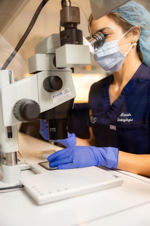 Lab technician in protective gear examines samples through a microscope in scientific research facility.
