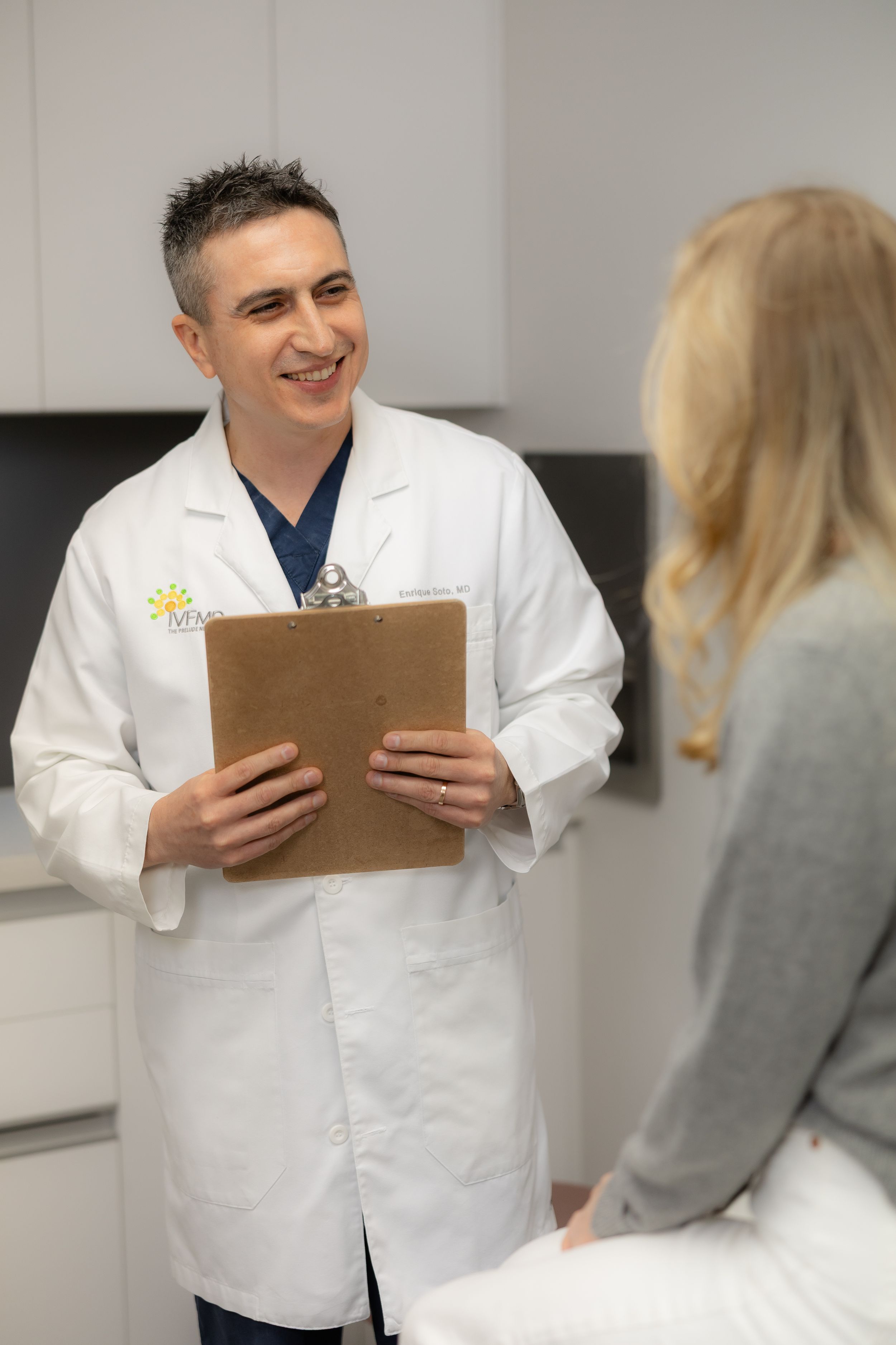 Medical professional consulting with patient in clinical setting while reviewing notes on clipboard.