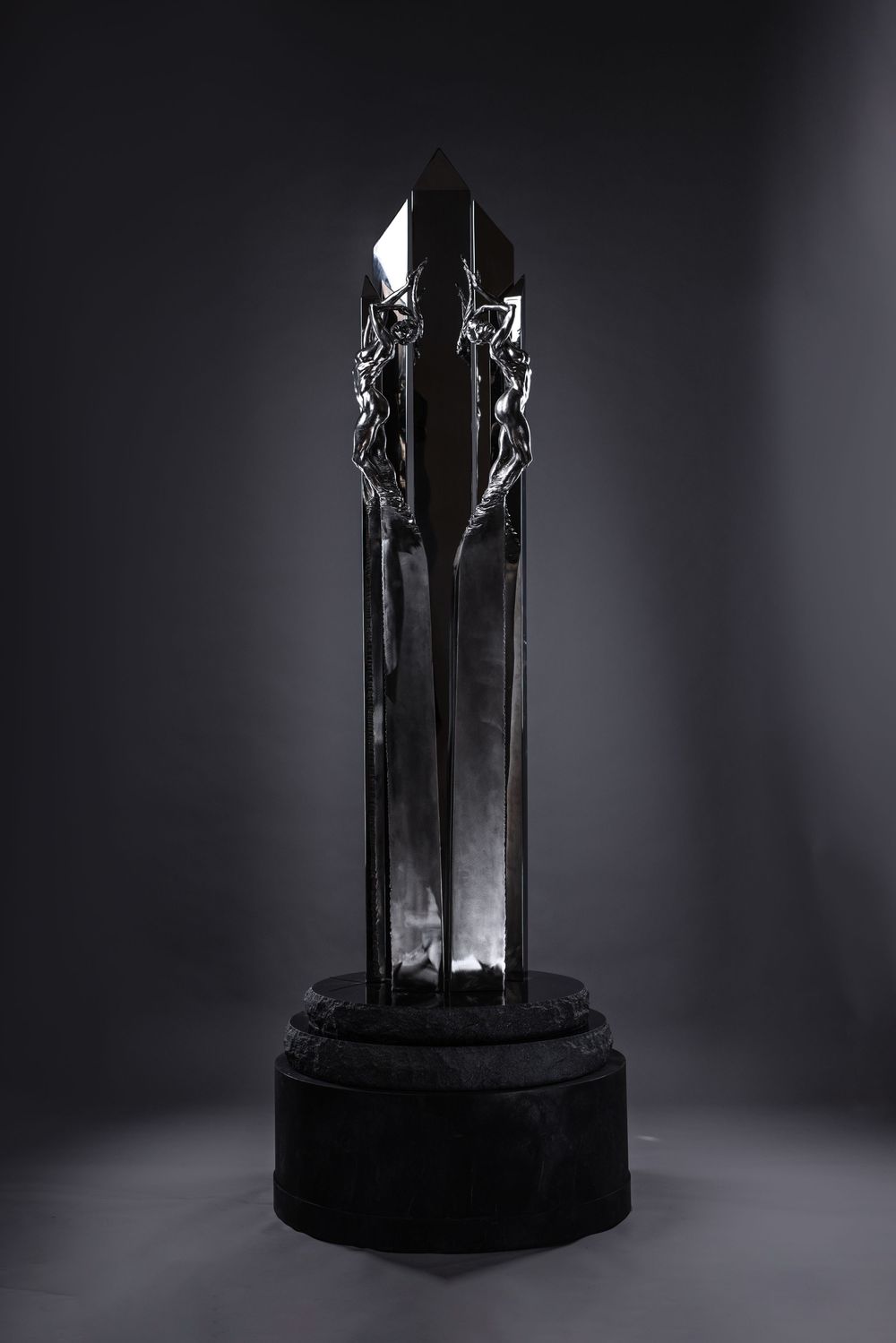 A black crystal trophy or award statue with angular geometric design stands dramatically lit against a dark background.