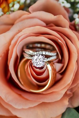 Wedding rings nestled inside a peach-colored rose, featuring a diamond engagement ring and gold wedding band.