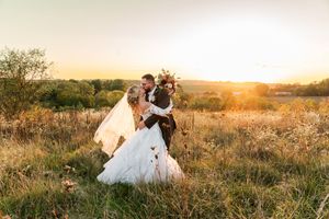 Romantic wedding couple embraces in golden sunlit field during sunset creating dreamy silhouettes.