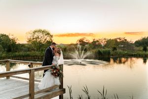 A couple poses for romantic sunset wedding photos on a rustic wooden dock overlooking a tranquil lake.