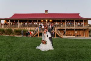 A panoramic view of a rustic barn wedding venue with a wooden exterior and expansive green lawn for outdoor ceremonies.