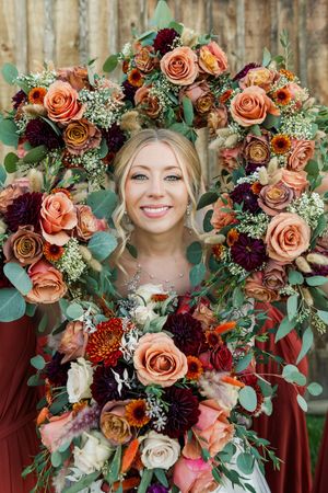 Romantic wedding bouquet features coral roses, burgundy flowers, and eucalyptus greenery in fall colors.