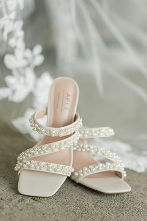 Elegant white pearl-embellished bridal sandals displayed against a soft neutral background.