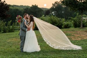 A couple embraces in a romantic moment outdoors with a flowing veil catching the breeze at sunset.