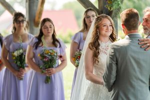 A wedding party stands in a line outdoors holding colorful bouquets while wearing formal attire.
