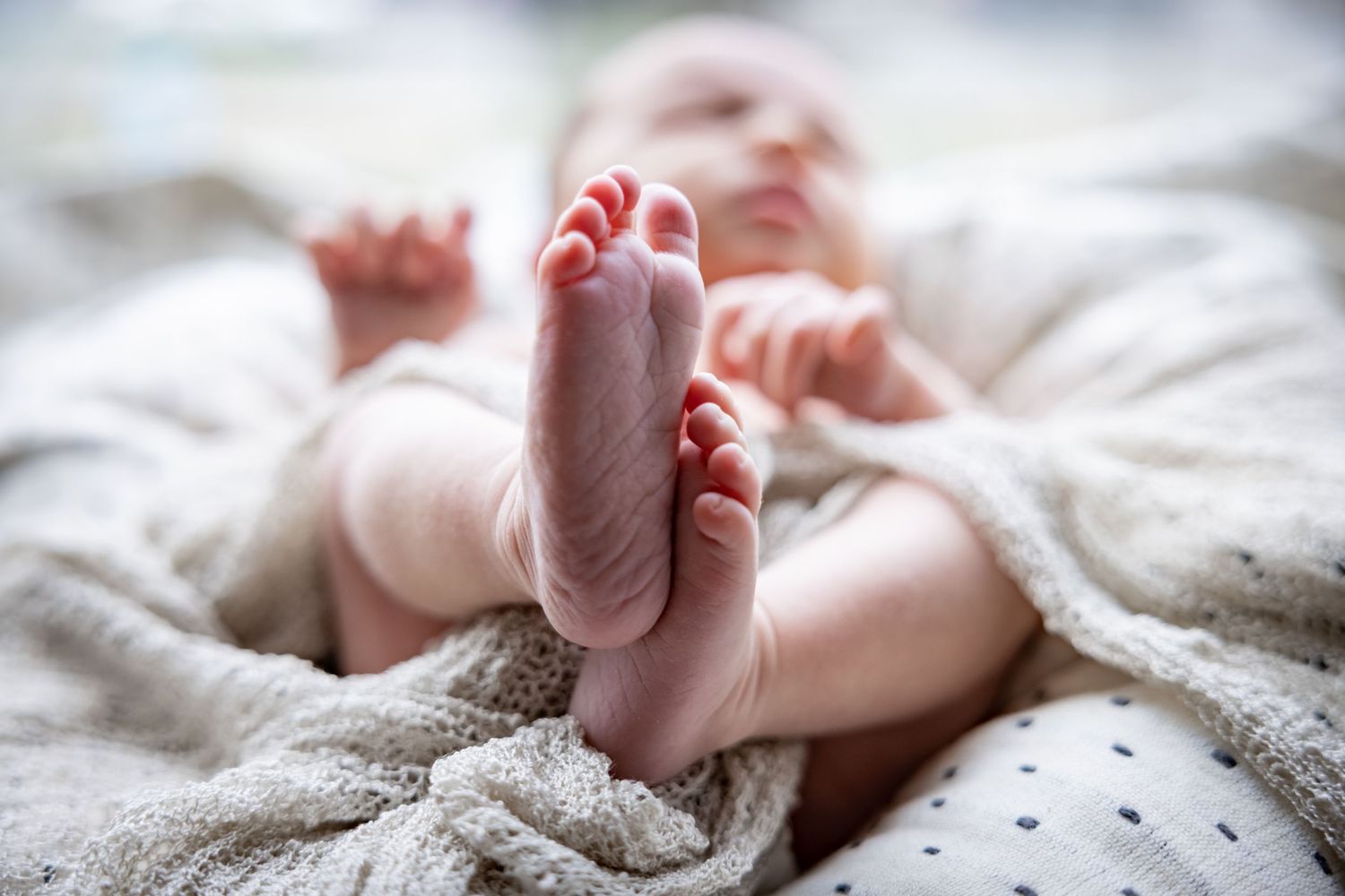 Close-up of adorable newborn baby feet resting on soft knit blanket in natural light.