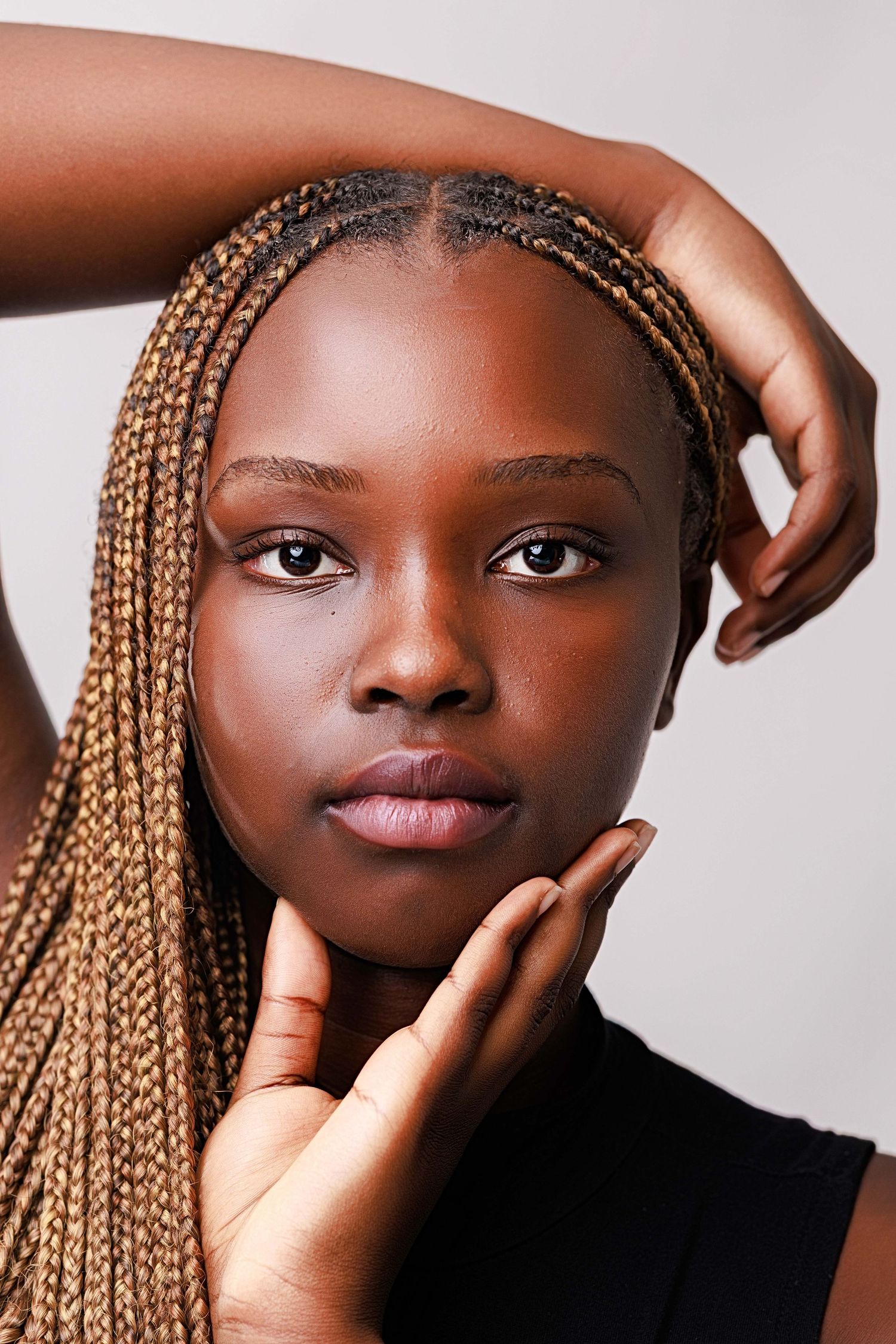 Young Black woman with long orange box braids poses gracefully, hands framing her face against a neutral background.