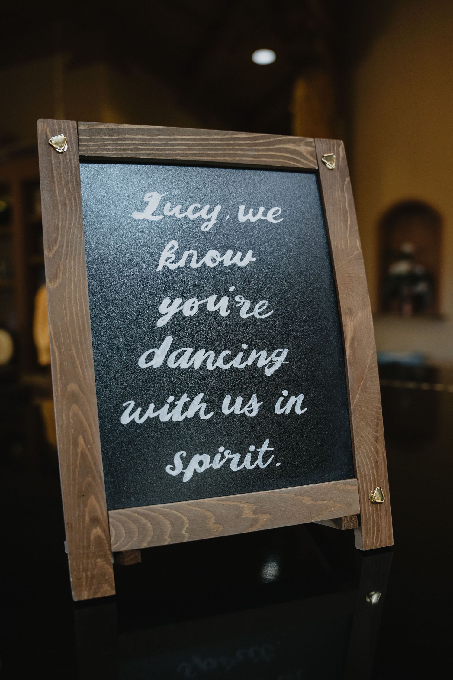 Chalkboard wedding sign reading Lucy we know youre dancing with us in spirit.