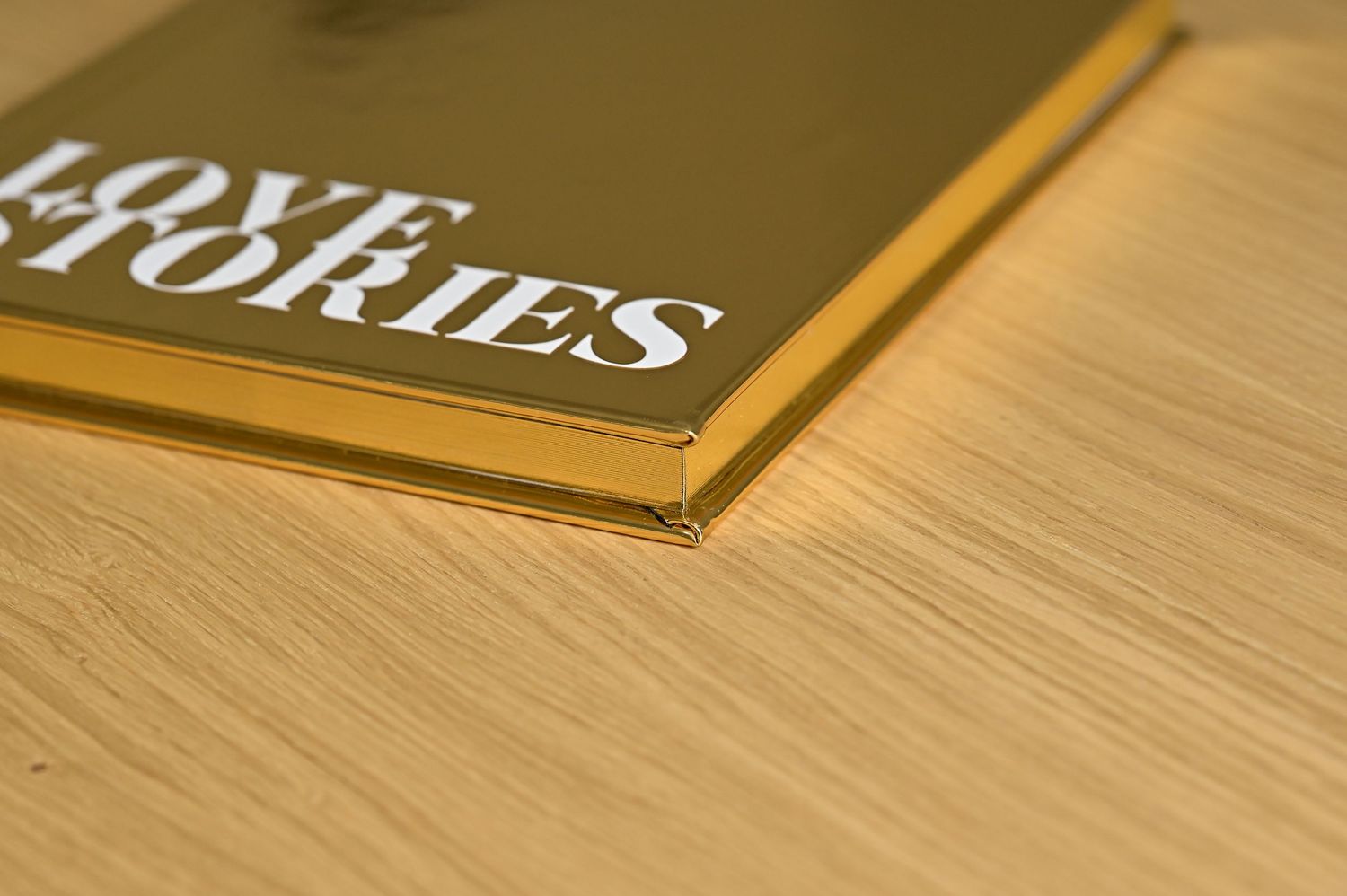 Close-up corner detail of a gold metallic Love Stories wedding photo album on wooden surface.