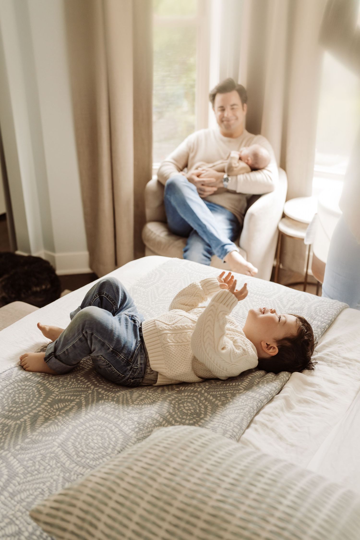 A toddler laughing on the bed during a lifestyle newborn session in Chicago.