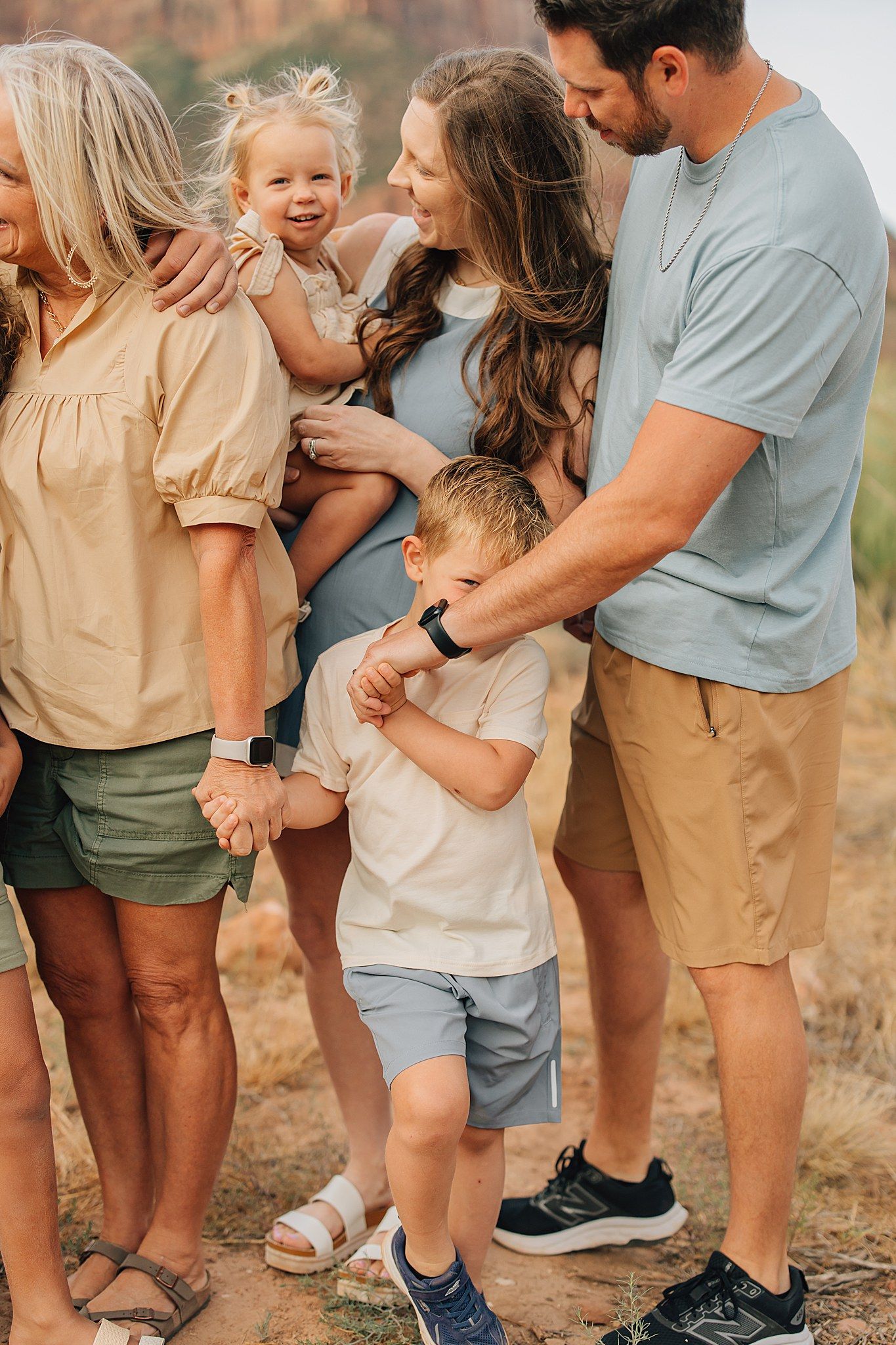 Multi-generational family portrait outdoors in natural desert landscape, parents with two young children smiling together.