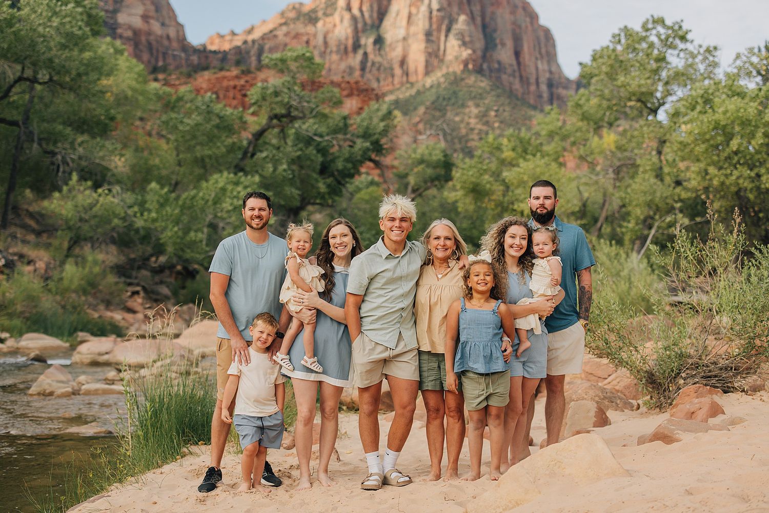 Large family posing together outdoors at Zion National Park with red rock canyon and lush greenery in background.