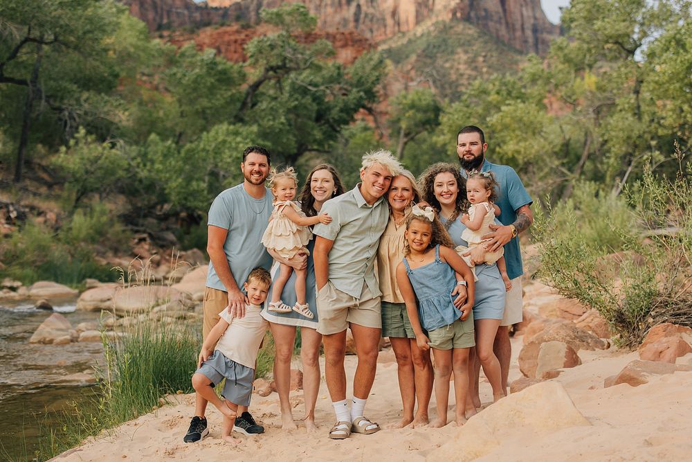 Large family posing together on rocky terrain at Zion National Park with red cliffs and lush greenery in background.