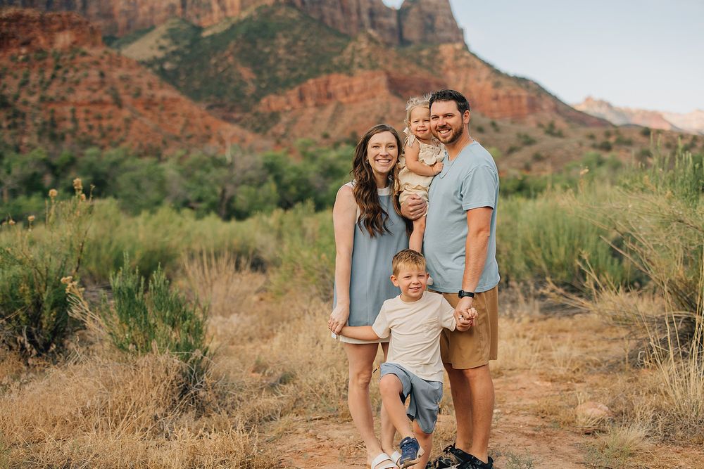 Family of four smiling outdoors in Sedona, Arizona, with red rock formations and desert landscape in the background.