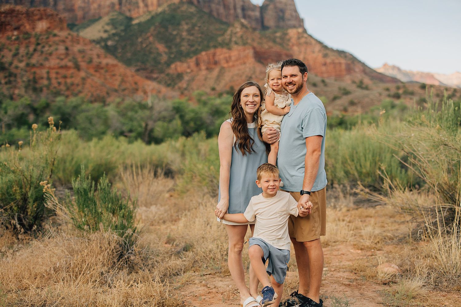 Family of four smiling outdoors in Sedona, Arizona, with red rock formations and desert landscape in the background.