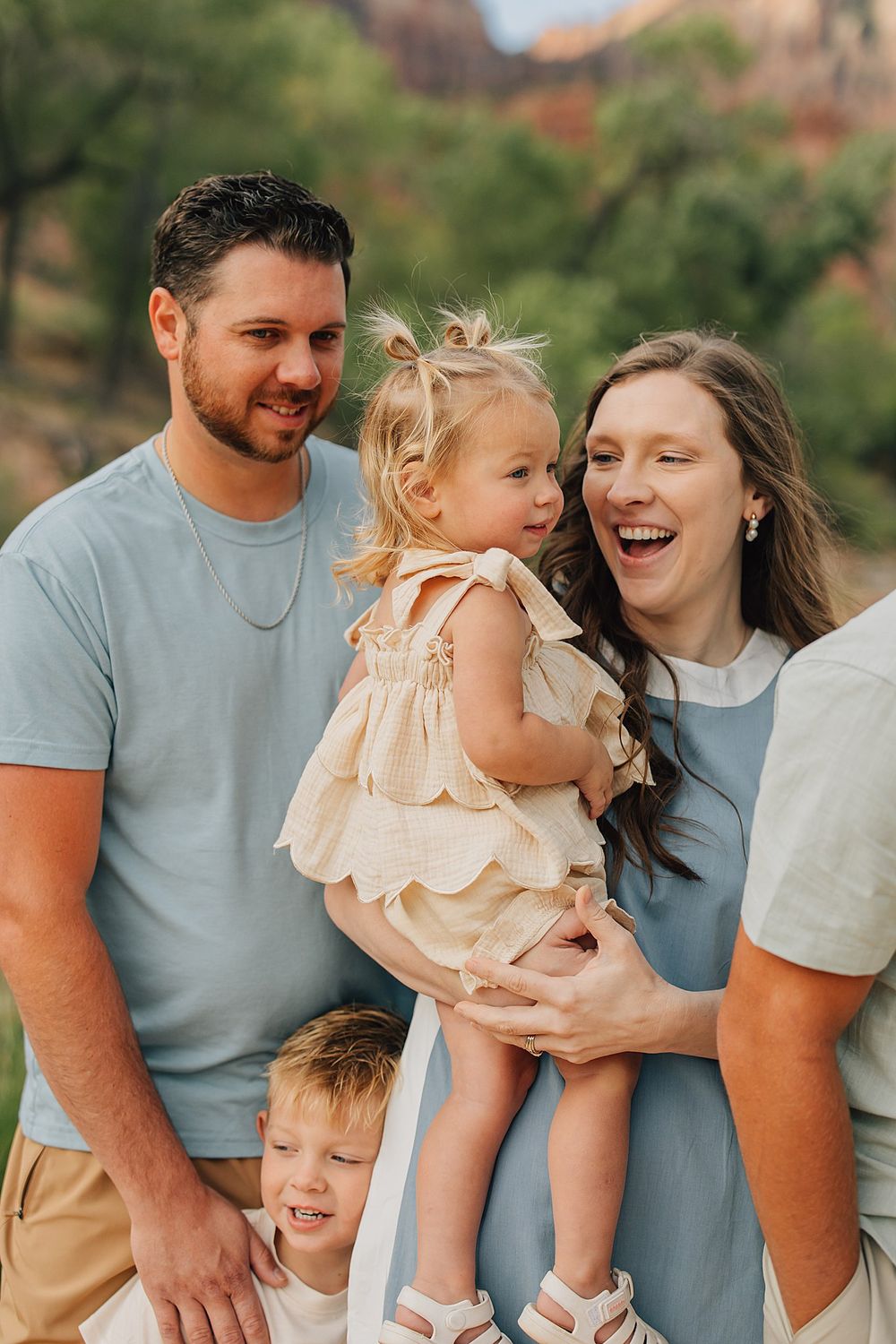 Happy family of four posing outdoors near red rock formations, parents smiling with two young children.